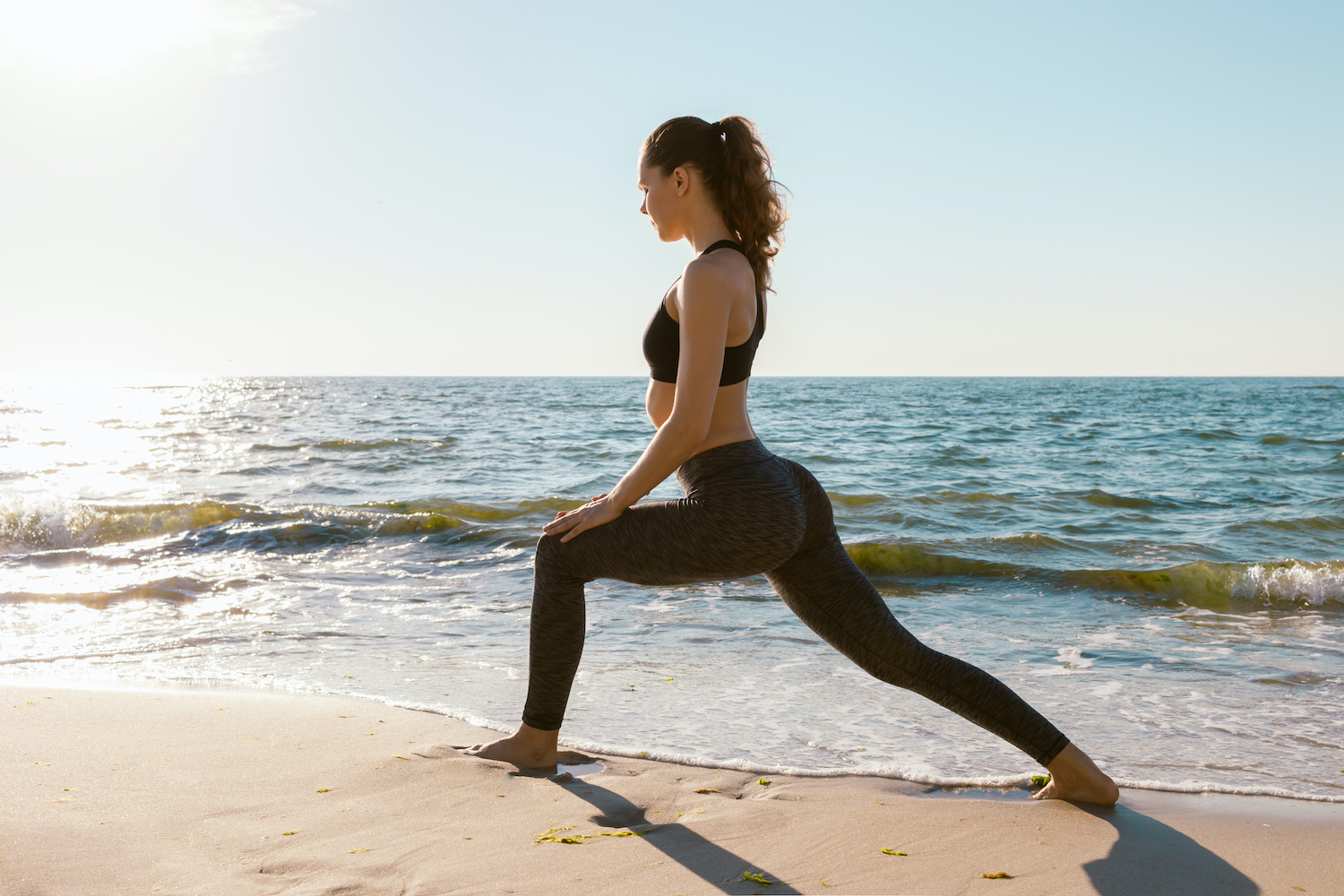Health conscious woman on a beach doing lunges exercises