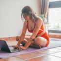 Young blond woman doing yoga and using her laptop in a studio
