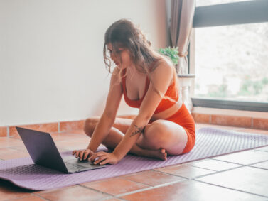 Young blond woman doing yoga and using her laptop in a studio