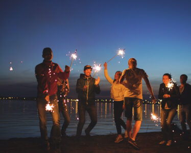 Young friends enjoying a beach party with sparklers in the early evening.
